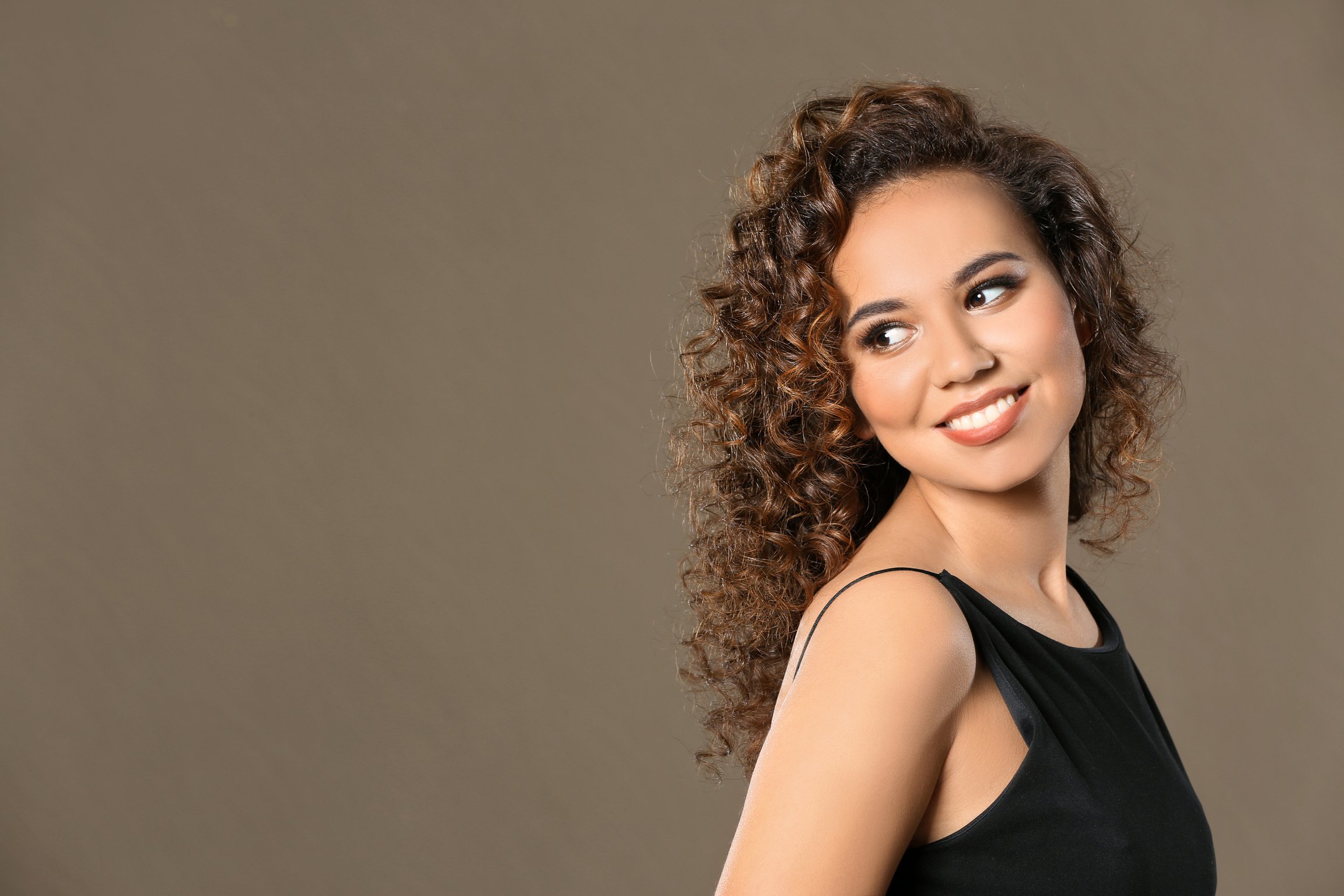 Beautiful Young Woman with Long Wavy Hair on Brown Background